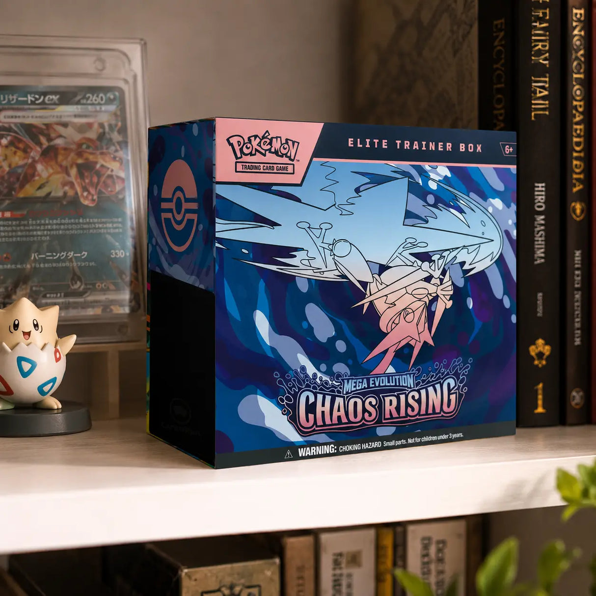 Pokemon Chaos Rising Elite Trainer Box – Lifestyle-Foto im Regal neben gegradetem Charizard ex und Togepi-Figur