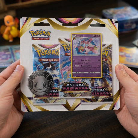 Hände halten Pokemon Astral Radiance Sylveon 3-Pack Blister mit Glumanda-Figur im Hintergrund