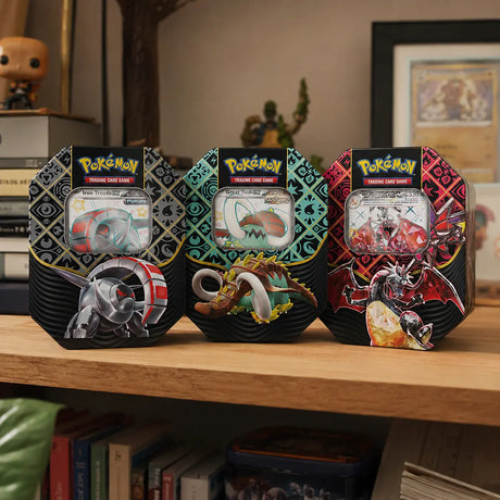 Pokemon Paldean Fates Tin auf Holzregal – Alle drei Varianten aufgereiht mit Funko Pop und Buecher im Hintergrund