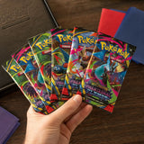 Hand hält 6 Phantasmal Flames Booster Packs aufgefächert vor Pokemon TCG Binder und Kartenhüllen