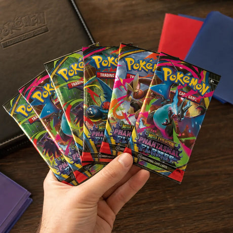 Hand hält 6 Phantasmal Flames Booster Packs aufgefächert vor Pokemon TCG Binder und Kartenhüllen