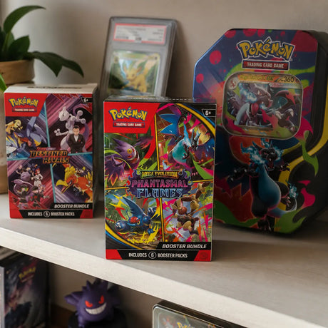 Pokemon Phantasmal Flames Booster Bundle auf einem Sammlregal neben Destined Rivals Bundle und Mega Glurak Tin