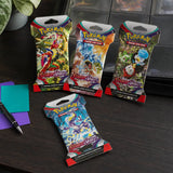 Vier Pokemon Scarlet & Violet Sleeved Booster Packs auf einem Schreibtisch mit Pokemon-Binder im Hintergrund