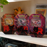 Alle 3 Pokemon Team Rocket Tins auf einem Sammlregal neben gegradetem Glurak und Pokemon-Figur
