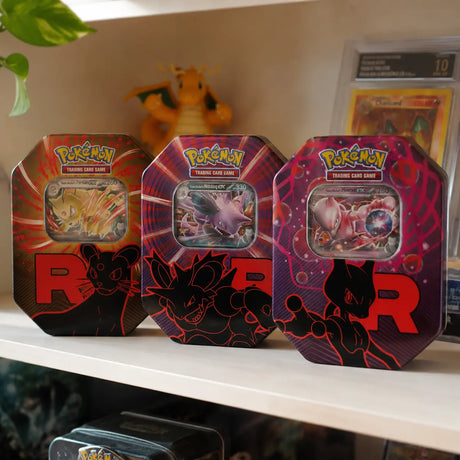 Alle 3 Pokemon Team Rocket Tins auf einem Sammlregal neben gegradetem Glurak und Pokemon-Figur