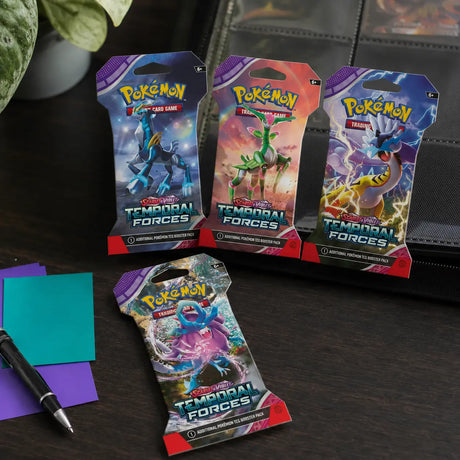 Vier Pokemon Temporal Forces Sleeved Booster Packs auf einem Schreibtisch neben Pokemon-Binder
